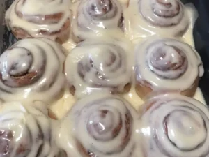 Freshly baked cinnamon rolls in a tray, covered with creamy glaze and swirled with cinnamon filling.