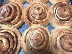 Freshly baked cinnamon rolls arranged on a baking tray, golden brown with visible swirls of cinnamon sugar.