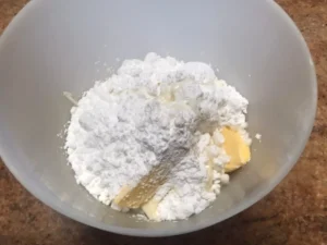 Bowl containing powdered sugar, butter, milk and cream cheese, ingredients for cinnamon roll icing.