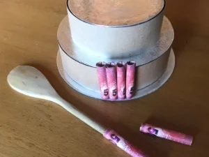 Partially decorated money cake with rolled banknotes and wooden spoon on the side.