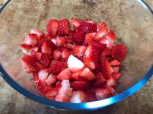 Bowl of freshly chopped strawberries in a clear glass bowl on a granite countertop.