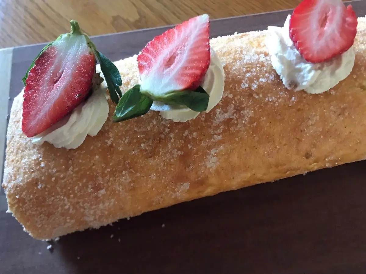 Close-up of a strawberries and cream Swiss roll topped with piped whipped cream and fresh strawberry halves.