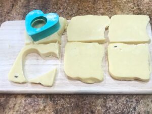 Shortbread dough sliced into squares with a heart-shaped cookie cutter