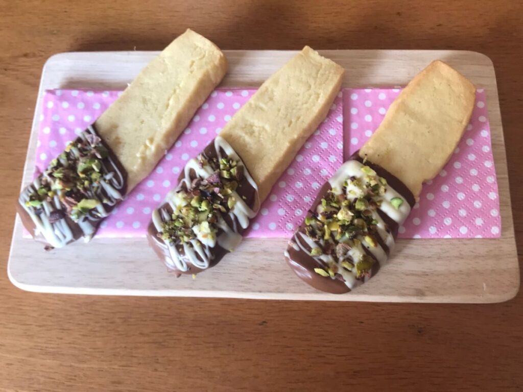 Baked shortbread cookies dipped in milk chocolate and drizzled with white chocolate and sprinkled with pistachios