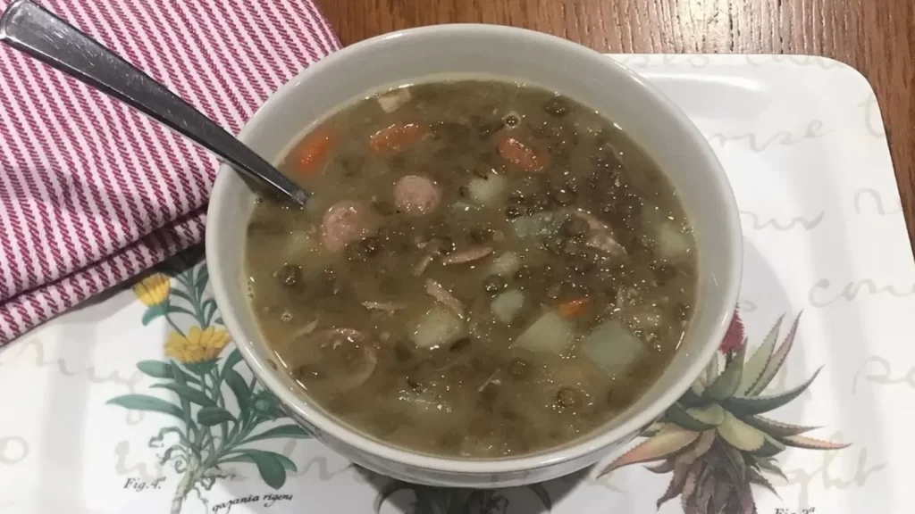 Bowl of homemade lentil soup with sausage, potatoes, and carrots on a decorative tray with a red-striped dish cloth.