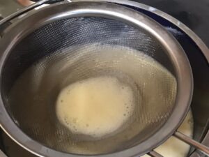 Pastry Cream Recipe - Warm milk being strained through a fine mesh sieve into a bowl.