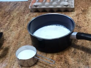 Pot of milk and a measuring cup of sugar on a kitchen counter ready for making a delicious Pastry Cream Recipe..