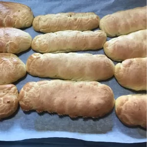 Freshly baked choux pastry éclairs on a lined baking tray, golden and puffed