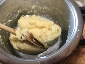 Choux pastry dough being stirred with a wooden spoon in a saucepan.