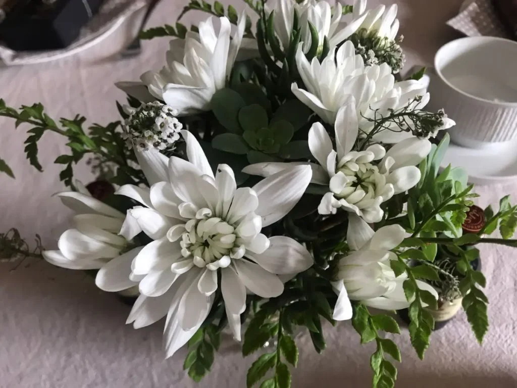 Elegant white flower arrangement with chrysanthemums and greenery in a neutral setting.