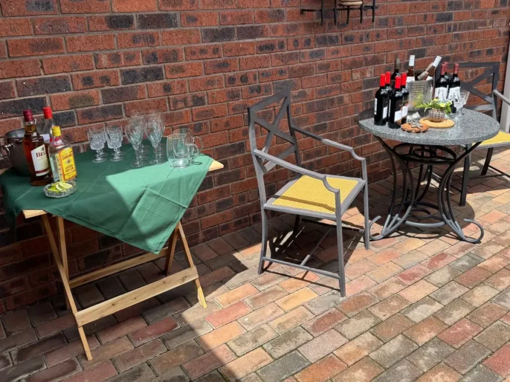Small outdoor drinks table with green tablecloth against brick wall for milestone birthday celebration