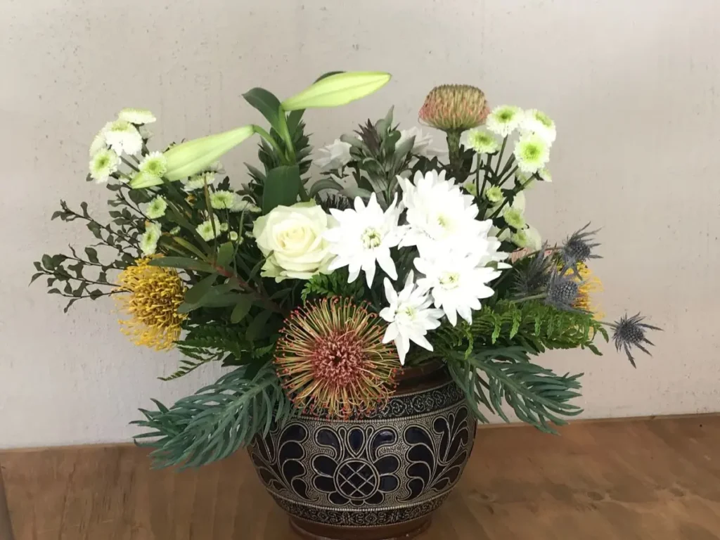 Elegant flower arrangement with white roses, proteas, and greenery in a patterned ceramic punch bowl.