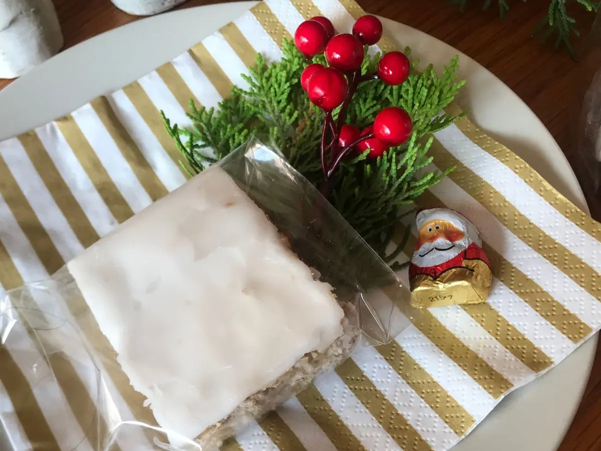 Pfefferkuchen vom Blech slice with icing in a cellophane bag and displayed on a white plate with gold and white striped servette some greenery and artificial berries and a small father christmas chocolate.