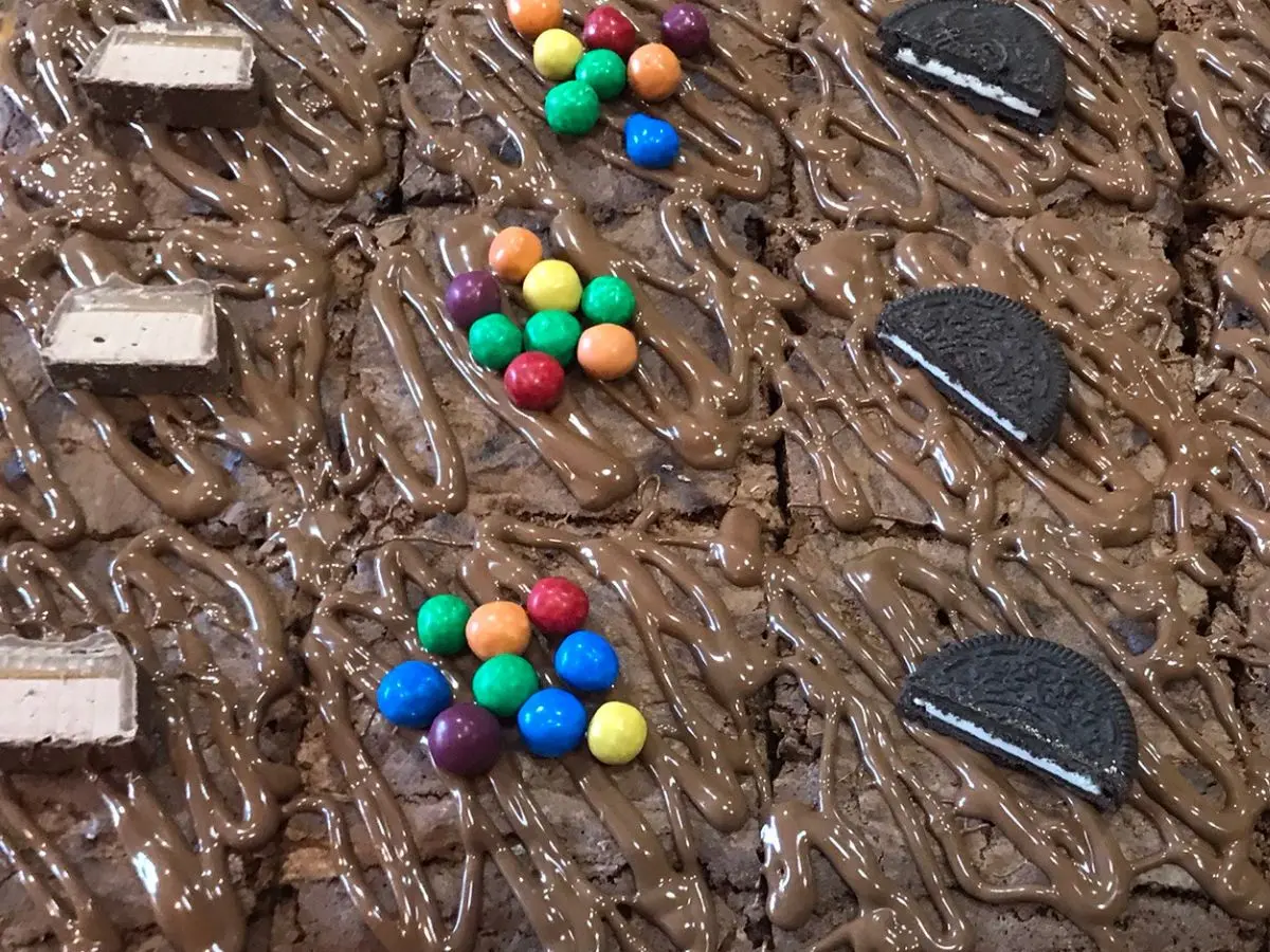 Chocolate brownies topped with drizzled chocolate and decorated with mini chocolate bars, colourful candy-coated chocolates, and Oreo halves.