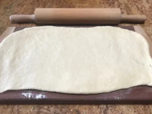 Rolled-out Butterkuchen yeast dough on a floured surface with rolling pin.