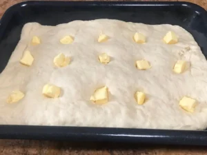 Butterkuchen dough pressed into a baking tray with small cubes of butter on top.