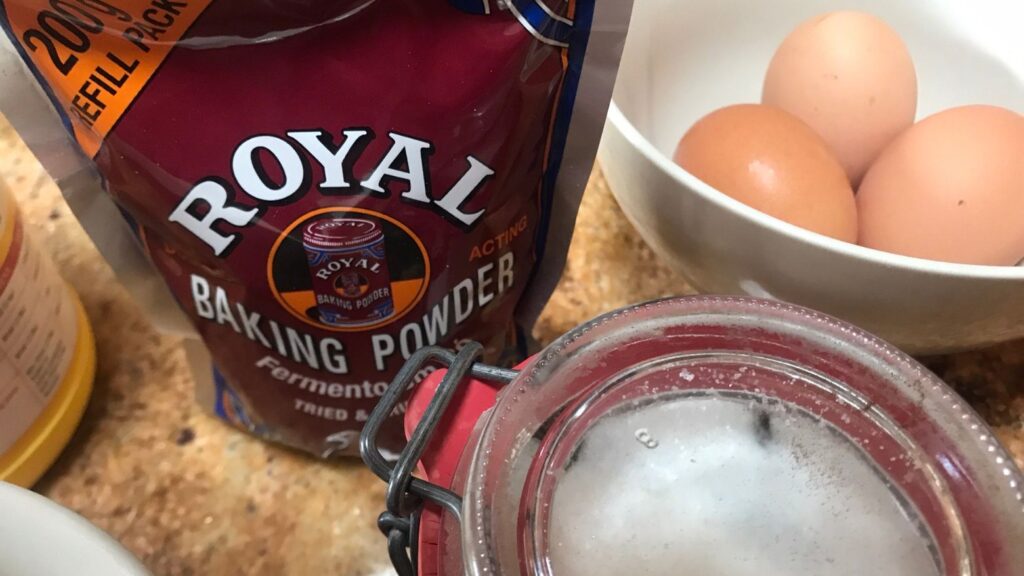 Glass jar of homemade vanilla sugar, baking powder, and fresh eggs on a kitchen surface