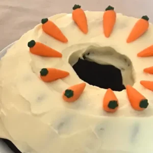 Ring-shaped carrot cake topped with cream cheese frosting and decorated with mini carrots.