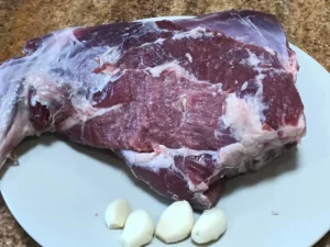 Raw leg of lamb with garlic cloves ready to be inserted