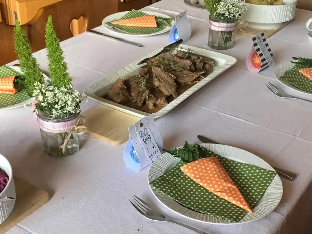 Easter table setting with carrot serviettes, leg of lamb and bunny arrangements