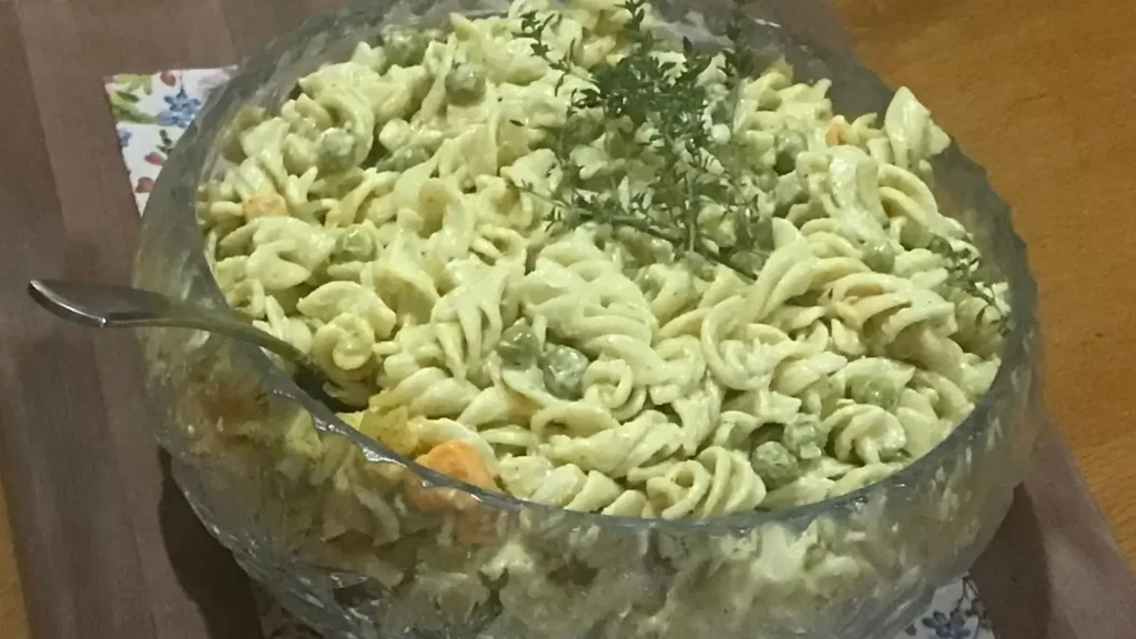 Creamy curried pasta salad with peaches and peas served in a glass bowl