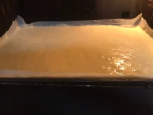 Swiss roll sponge batter baking on a lined tray in the oven.