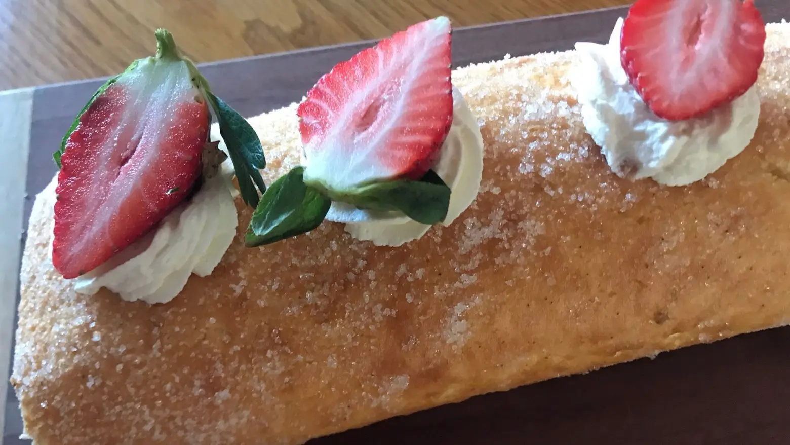 Close-up of a strawberries and cream Swiss roll topped with piped whipped cream and fresh strawberry halves.