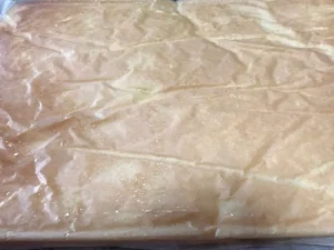 Swiss roll sponge turned out onto sugared paper with baking paper still on top, ready to be peeled off.
